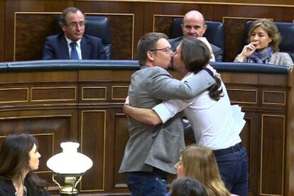 Imagen tomada de la señal institucional del Congreso de los Diputados en la que aparecen el líder de Podemos, Pablo Iglesias (d), y el de En Comú Podem, Xavier Doménech, celebrando su estreno hoy en la tribuna de oradores de la Cámara Baja con un efusivo abrazo y un beso en los labios.