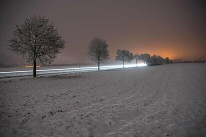 La luz de los coches coches forma una estela de luz en un camino rural con nieve en Vaterstetten, cerca de Múnich (Alemania).