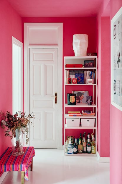 El núcleo de color de la casa es el pasillo, que decidieron que fuera de rosa magenta. Se prefirió pintar una zona de paso para que el color no abrumara. En la pared de la derecha, un cuadro de Enrico de Paris. Sobre la estantería, una cabeza de Adan, un diseño de Teresa Sapey. Abajo, el minibar.