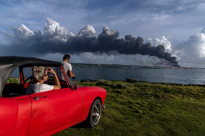 El fuego se expande en esta ciudad costera, 90 kilómetros al este de La Habana, donde al menos tres tanques de crudo arden en llamas tras el impacto de un rayo en la noche del viernes. En la imagen, dos personas observan una enorme columna de humo que se eleva desde el depósito de combustible de Matanzas.
