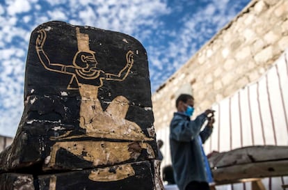 Um visitante tira fotos ao lado de um sarcófago de madeira descoberto na necrópole de Saqqara. Os caixões encontrados são antropomórficos e decorados com cenas de divindades e textos funerários.