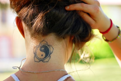 A girl shows the tattoo se has on the back of her neck.