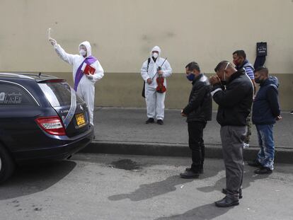 Un clérigo rocía agua bendita mientras familiares se reúnen alrededor del coche fúnebre que transporta a una víctima del COVID-19 al cementerio Chapinero en Bogotá, Colombia, el pasado 6 de agosto de 2020.