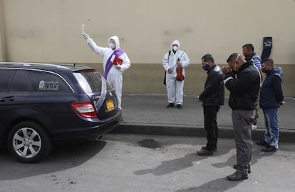 Un clérigo rocía agua bendita mientras familiares se reúnen alrededor del coche fúnebre que transporta a una víctima del COVID-19 al cementerio Chapinero en Bogotá, Colombia, el pasado 6 de agosto de 2020.