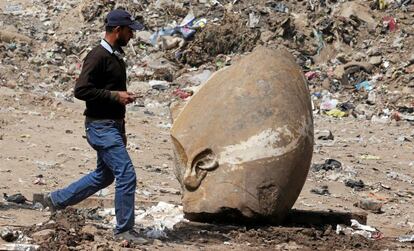 Un hombre pasa junto a la cabeza de la estatua hallada este jueves en una excavaci&oacute;n en El Cairo. 