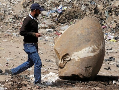 Un hombre pasa junto a la cabeza de la estatua hallada este jueves en una excavaci&oacute;n en El Cairo. 