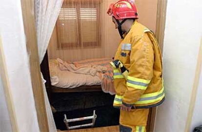 Un bombero observa el agujero que se abrió bajo la cama de la anciana que resultó herida grave.