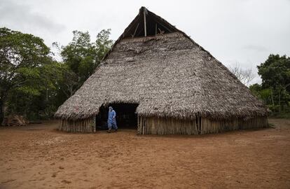 Un miembro del personal de vacunación sale de una maloca (vivienda de madera típica de la Amazonía). La inmensidad del bosque lo acompaña.