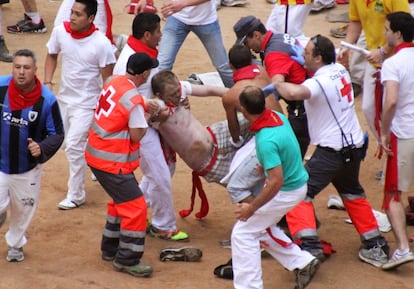 Corredores del encierro y personal sanitario trasladan a uno de heridos en el montón de mozos formado en la entrada a la plaza de Pamplona.