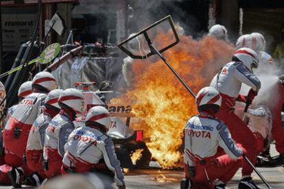 Los operarios apagan las llamas en torno al coche de Jarno Trulli al prenderse la gasolina caída al asfalto.