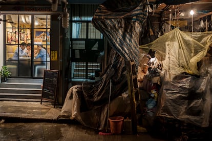 'Vivienda'. Un hombre prepara su tienda callejera como dormitorio frente a un restaurante en Hong Kong. 2014
