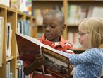 Un niño y una niña leen un cuento en una biblioteca. 