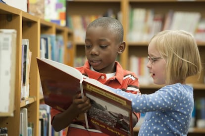 Un niño y una niña leen un cuento en una biblioteca. 