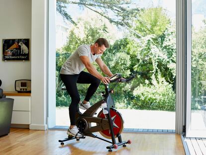 Un hombre hace ejercicio en una bicicleta estática, en el salón de su casa