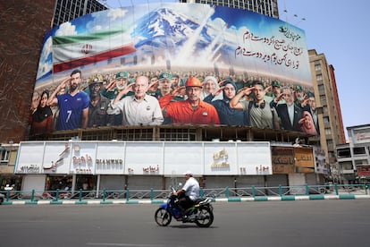 Un hombre en motocicleta pasa junto a una valla publicitaria que muestra a varios iraníes, incluyendo militares con el lema "Todos somos soldados de Irán", en la plaza Vali-Asr de Teherán. este domingo.