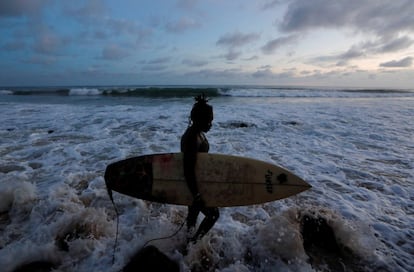 Khadjou Sambe lleva su tabla de surf mientras camina junto al mar en la llamada Playa Secreta de Dakar, Senegal, el 14 de agosto de 2020. Esta es más adecuada para surfistas experimentados.