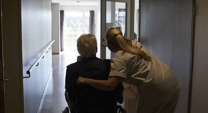 Una trabajadora, junto a un hombre en silla de ruedas, en una residencia.