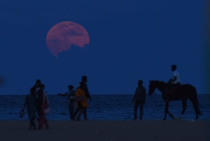 Um homem monta a cavalo junto a um grupo de pessoas que olha a Lua sobre a praia de Chennai (Índia).