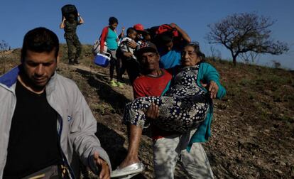 Un hombre ayuda a una mujer a cruzar la frontera entre Venezuela y Brasil.