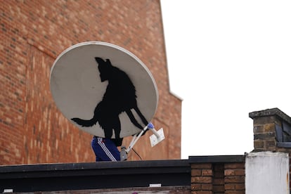 Un individuo retira la nueva pieza de Banksy de un lobo sobre una antena parabólica el jueves 8 de agosto en Peckham, Londres.