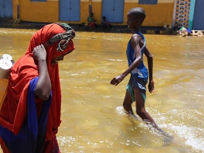 Una mujer y un niño caminan entre el agua tras una inundación.