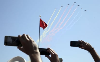 Asistentes al desfile fotografían con sus teléfonos móviles a los aviones de combate que sobrevuelan la plaza de Tiananmen, en Pekín.