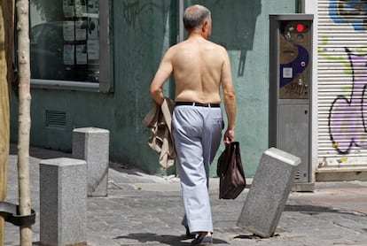 Un hombre pasea sin camisa con un maletín por una calle de Madrid