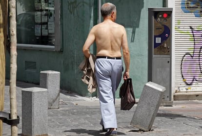 Un hombre pasea sin camisa con un malet&iacute;n por una calle de Madrid