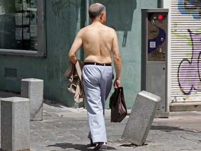 Un hombre pasea sin camisa con un malet&iacute;n por una calle de Madrid