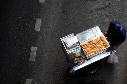 Un vendedor empuja su carrito de comida en busca de clientes a lo largo de una calle en Bangkok.