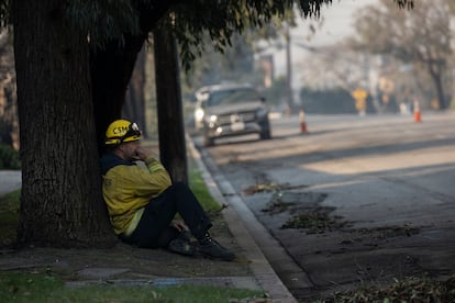 Un bombero descansa en el suelo mientras varios de sus compañeros refrescan un edificio humeante en una calle de Pacific Palisades, en Los Ángeles. 