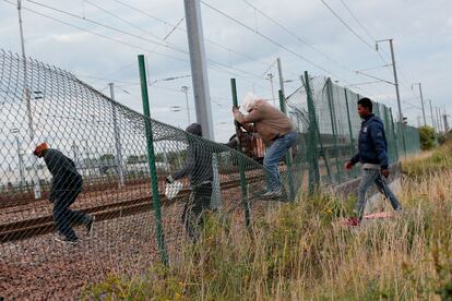 Inigrantes pasan por encima de una valla para entrar en el área del Eurotunnel, en Calais.