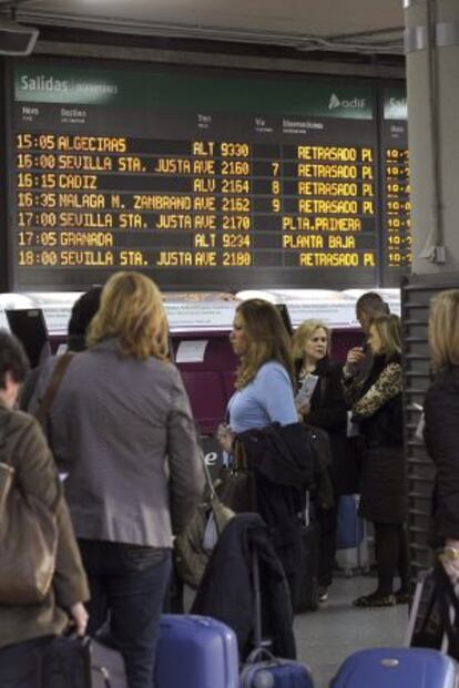 Varias personas esperan en la estaci&oacute;n de Atocha, en Madrid, ante un panel que informa del retraso de los trenes.