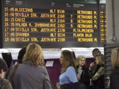 Varias personas esperan en la estaci&oacute;n de Atocha, en Madrid, ante un panel que informa del retraso de los trenes.
