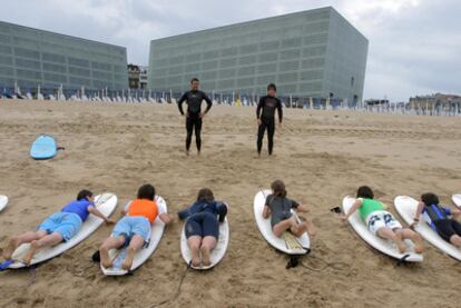 Los alumnos de una escuela de surf en la playa de Zurriola, con el Kursaal al fondo.