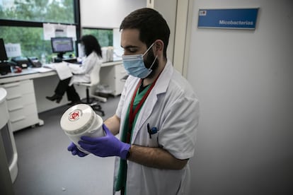 <p>En el laboratorio, entre campanas de presión negativa, cámaras de frío y máquinas dedicadas exclusivamente a determinar el negativo o positivo de las centenares de muestras que les llegan a diario, decenas de técnicos y microbiólogos trabajan desde hace más de un mes. En la imagen, Agustín Estévez, residente de segundo año de Microbiología, muestra uno de los recipientes donde llegan las muestras. Poco después, se mete en una de las salas del proceso para determinar si esa muestra será o no portadora de coronavirus; en la puerta de esa sala, hay un dibujo con un cerdito pegado. Tiene que ver con un aparato circular que Estévez dice que los tiene "enamorados".</p><p>Esa máquina es para procesos en sanidad animal, cuenta el microbiólogo Roberto Alonso, y se la cedió una de las casas comerciales con la que trabajan, en Lyon. "Nos dijeron que nos la enviaban en 24 horas, pero que no podían instalarla porque su personal técnico no estaba autorizado a viajar". Patricia Muñoz, la jefa de servicio, encontró la soluciön: "Llamé a un amigo mío muy mañoso que acababa de llegar del Congo de montar un hospital de campaña, trabaja en un taller con piezas de coche. Le hicimos un salvoconducto y Nacho nos la montó con un vídeo que nos enviaron los de Lyon".</p>