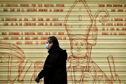 Mulher caminha diante de grafite com mensagens religiosas que pedem proteção em diversas línguas, em Pamplona, na Espanha.