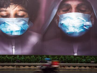 Un repartidor pasa junto a una valla publicitaria instando a las personas a utilizar mascarillas en Dubái (Emiratos Árabes).