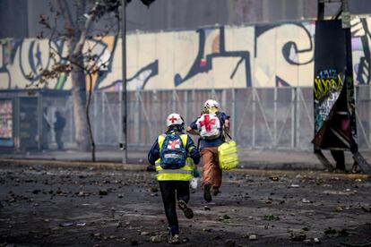 Dos voluntarios corren para protegerse en medio de una protesta en Santiago.