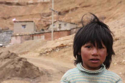 Retrato de una niña en la ladera de la montaña con un campamento minero en el fondo.