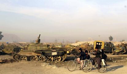 Niños afganos pasan junto a tanques que fueron utilizados durante la Guerra de Afganistán abandonados en un desguace en Kandahar (Afganistán).