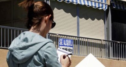 Una joven junto a un cartel que anuncia un piso para alquilar.