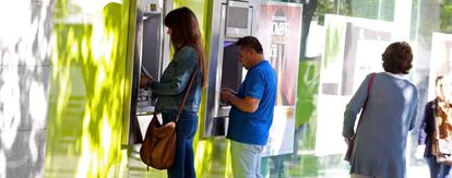 Varias personas sacan dinero de un cajero automático de Bankia.