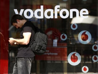 Un hombre consulta su tel&eacute;fono junto a una tienda de Vodafone.