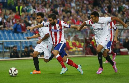 El judador del Atl&eacute;tico Arda Turan se abre paso entre dos jugadores del Sevilla.