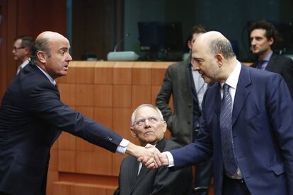 Luis de Guindos, estrecha la mano del comisario Pierre Moscovici en presencia del ministro alem&aacute;n de Econom&iacute;a, Wolfgang Schaeuble.