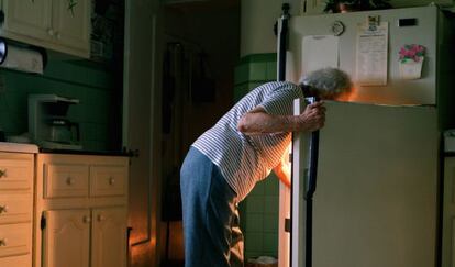 Una mujer mayor mira en la nevera de su casa.