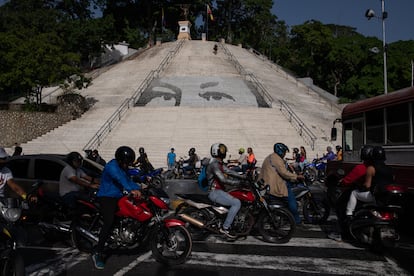 Motociclistas pasan frente a una escalera con un mural de los ojos de Hugo Chávez en el Parque Calvario en Caracas, en junio de 2022.