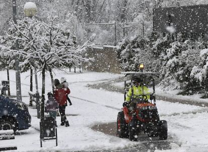 Un pequeño tractor retira la nieve acumulada en el acceso a un colegio de la localidad navarra de Uharte mientras un padre acerca a sus hijos al centro escolar en medio de la nieve.