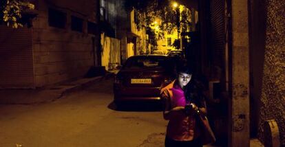 Una chica utiliza su m&oacute;vil en una calle mal iluminada en Delhi. 